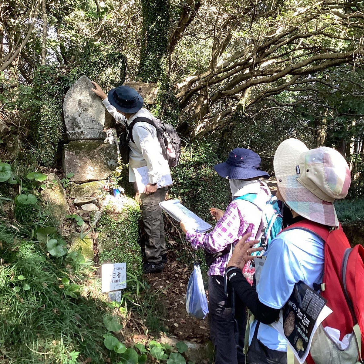 山中の石仏をトレッキングスタイルの男女3人が調査している